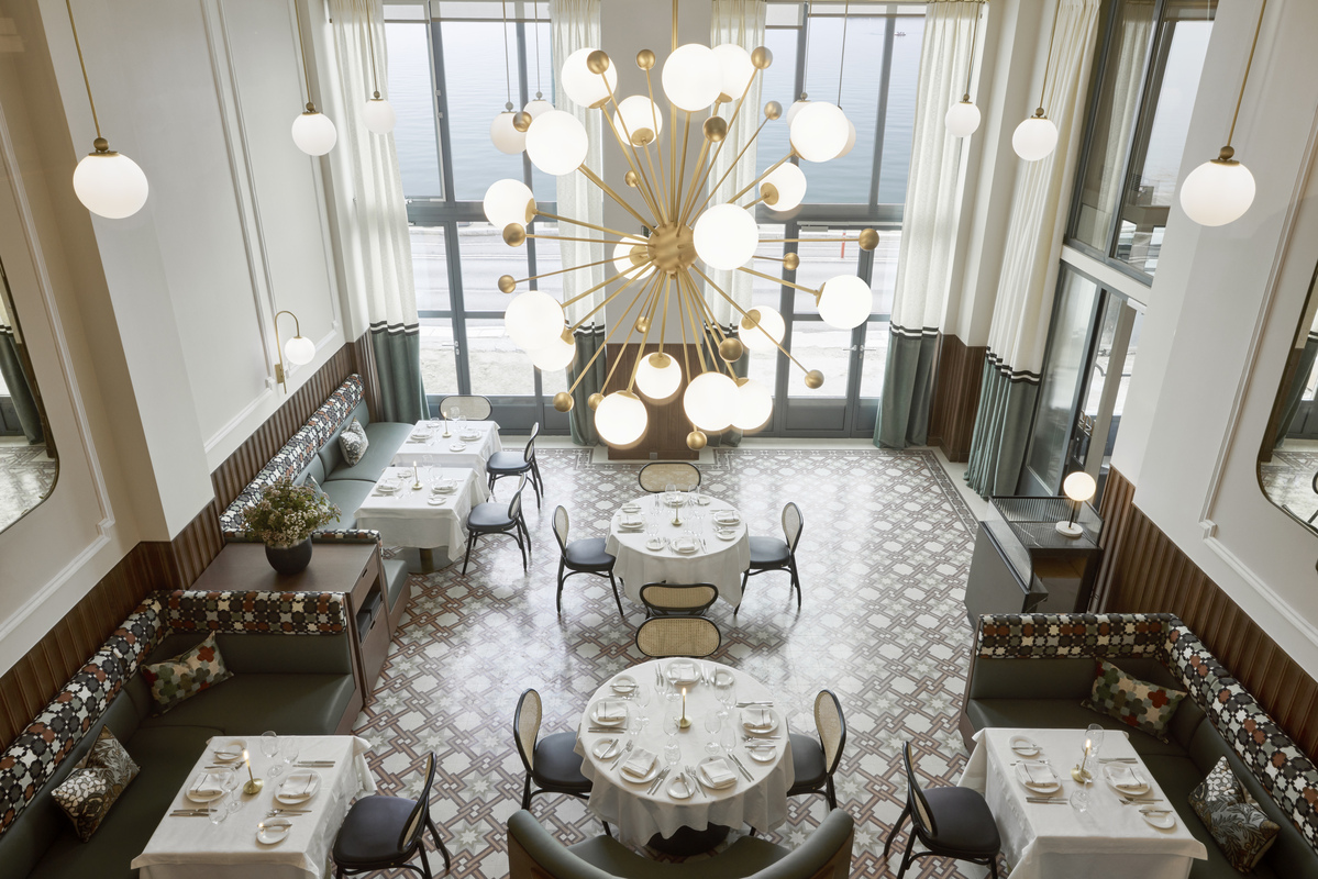 Stylish interior of Olympos Naoussa restaurant featuring patterned floors, round tables, booth seating, and a modern chandelier