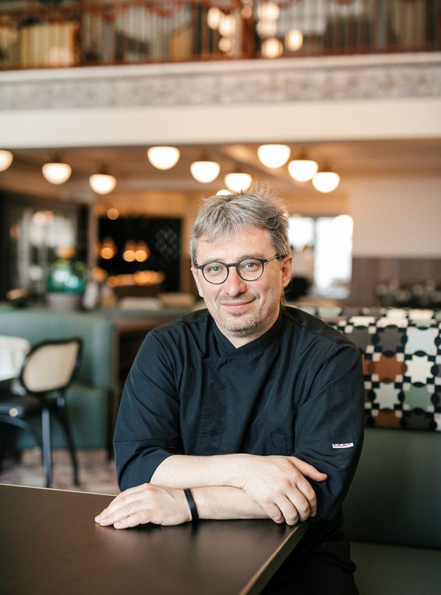Chef seated in Olympos Naoussa restaurant dining area wearing black uniform