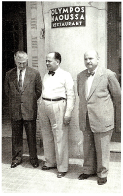 Olympos Naoussa owners standing outside the restaurant entrance, dressed in suits